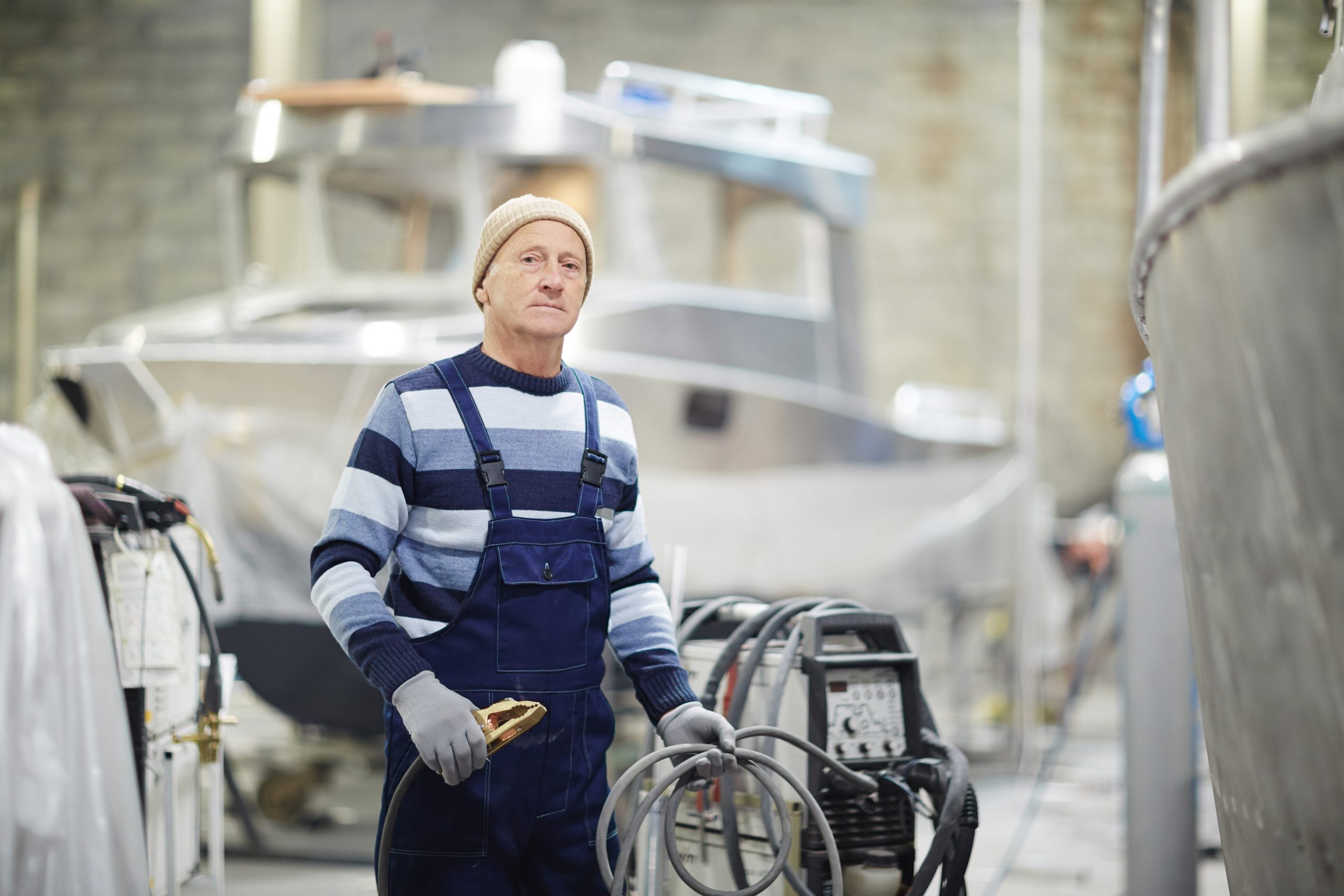 Ingénieur mature en vêtements de travail tenant un tuyau en caoutchouc tout en travaillant à l'intérieur d'un chantier naval
